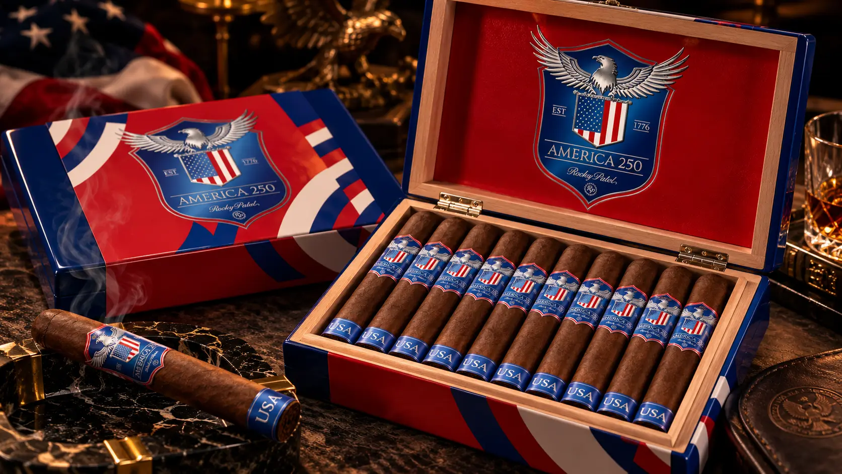 An open box of Rocky Patel America 250 in red, white and blue with an eagle emblem, next to a cigar with a USA band